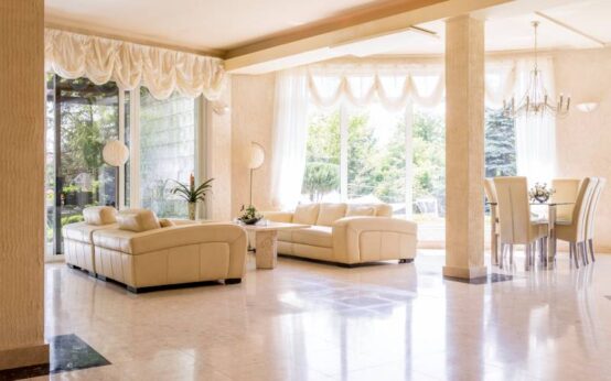 Bright, marble designed living room, surrounded by windows, with large sofa, armchairs, dining space with chairs and the chandelier