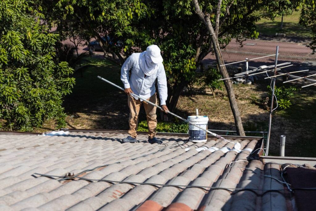 Worker adding undercoat foundation paint onto rooftop with roller as primer at residential building in renovation
