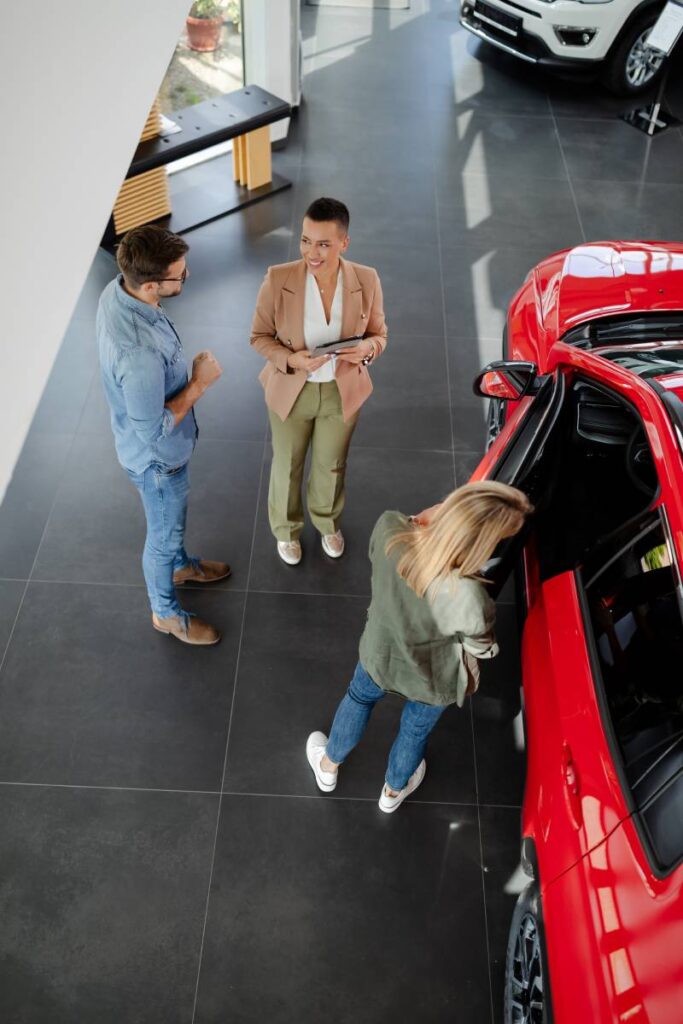 Top view of young couple choosing and buying car at car showroom. Car saleswoman helps them to make right decision.