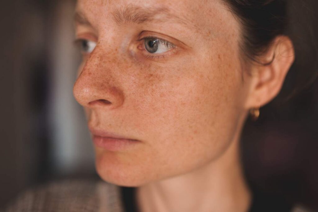 Closeup portrait of young waman with freckles and healthy natural skin indoors. Wellness. 20s. Selective focus.