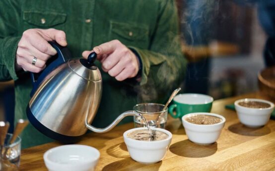 Man pouring boiling water into coffee bowls for tasting on coffee shop counter